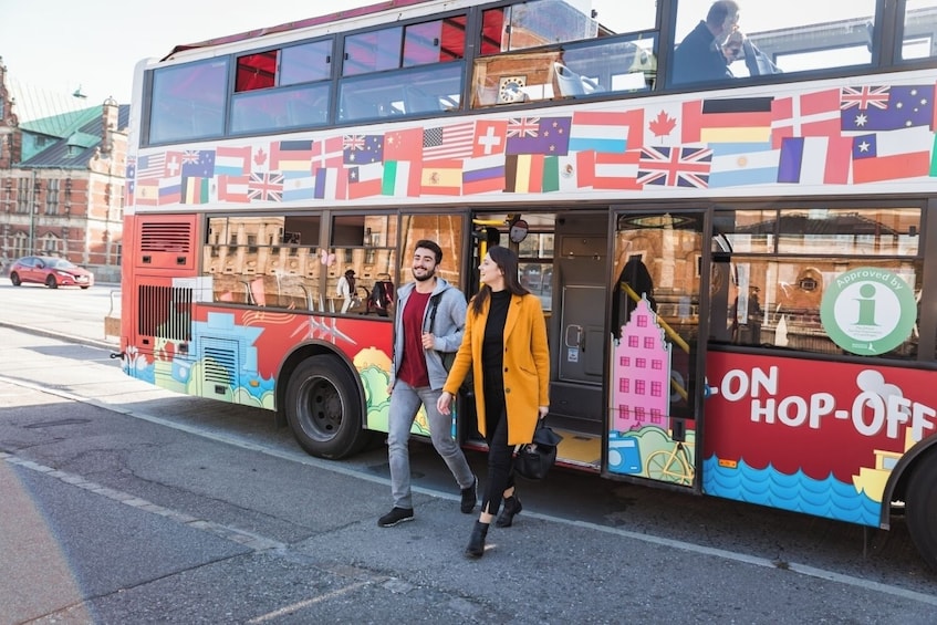 Un autobús de dos pisos con banderas internacionales de colores y un letrero que dice 'HOP-ON-HOP-OFF'. 4