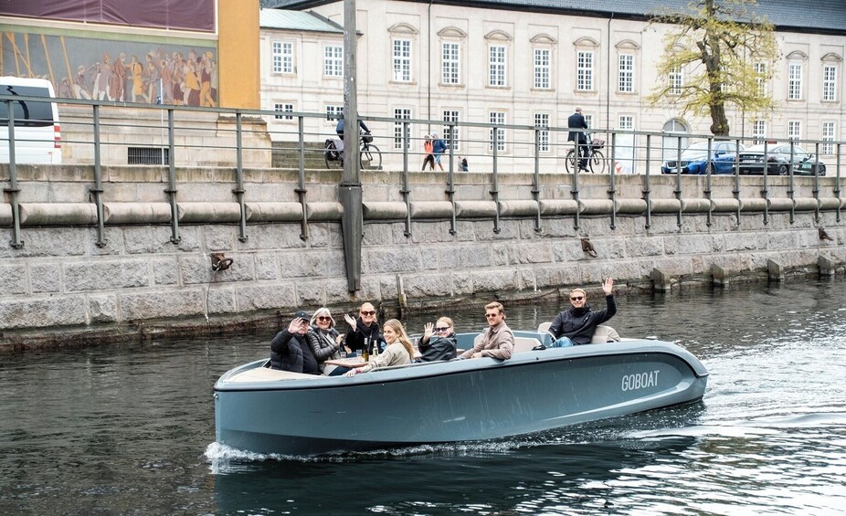 Un grupo de personas en un barco llamado 'GOBOT' navegando por un canal, con edificios y un puente al fondo. 3