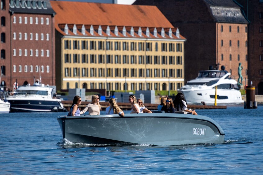 Un barco motorizado llamado 'GOBOAT' con pasajeros en el agua, barcos amarrados y edificios al fondo. 2