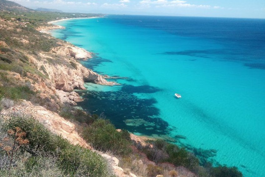 A coastal landscape with clear turquoise waters, rocky cliffs, and sparse vegetation. 3