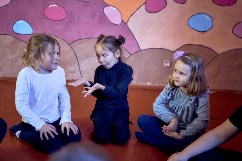 Three children sitting on the floor in a room with a colorful wall mural. 4