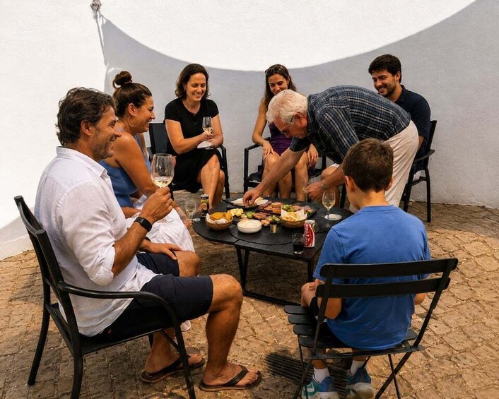 A group of people sitting around a table with food and drinks, outdoors on a patio. 2