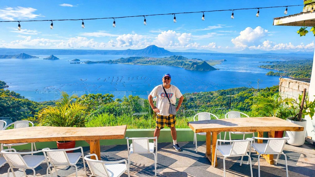 A man standing on a terrace overlooking a coastal landscape with mountains and a view of the sea. 3