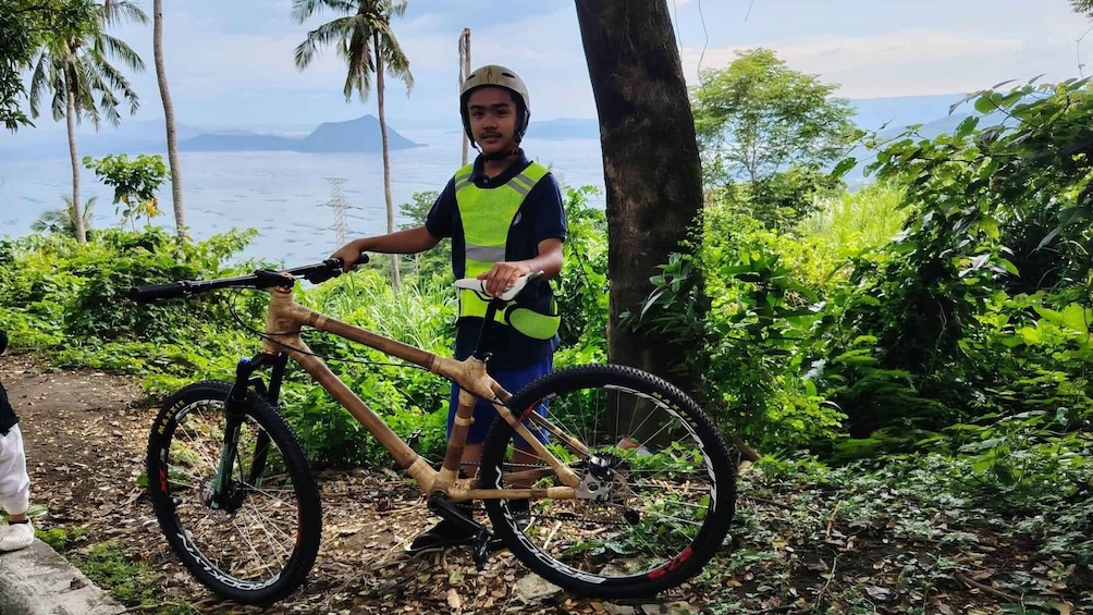 A person standing next to a mountain bike in a forested area with a view of the ocean in the background. 3