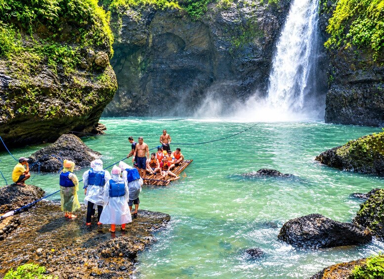 A group of people on a boat in a river with a waterfall in the background. 1