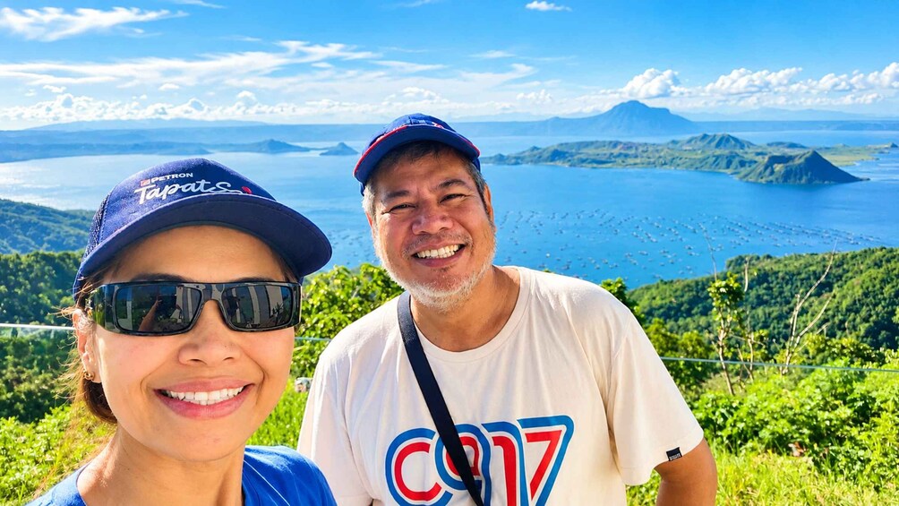 Two people standing on a hill with a view of a large body of water and mountains in the distance. 5
