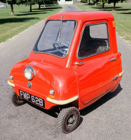 A red vintage car parked on a paved road with grass and trees in the background. 4