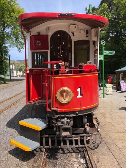 A red and white vintage tram with the number 1, parked on tracks with a green signpost in the background. 2