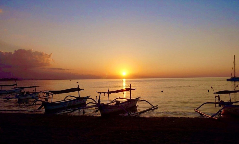 A sunset over a calm sea with several boats anchored near the shore. 3