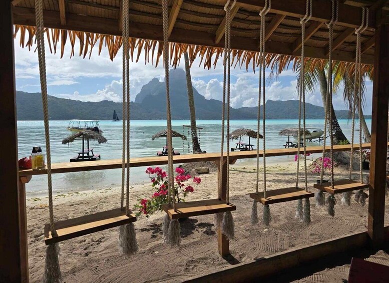 A beach with wooden swings and thatched umbrellas, overlooking a calm sea and distant mountains. 1