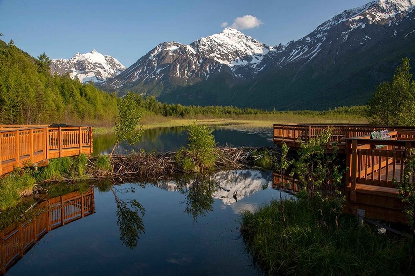 A wooden bridge over a calm lake with snow-capped mountains in the background. 4