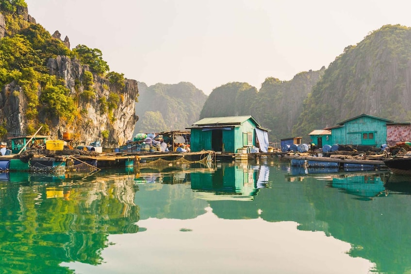 Un plan d’eau paisible, avec des bateaux, des constructions en bois et de hautes falaises verdoyantes. 3