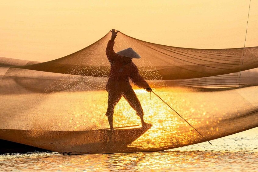 Une personne vêtue d’un costume traditionnel, debout sur un bateau et tenant un filet de pêche. 1