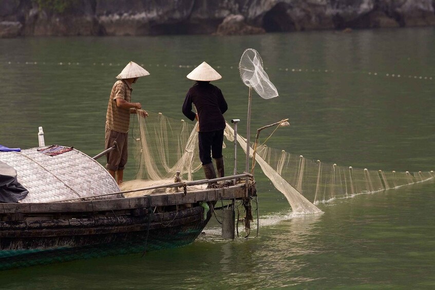 Deux personnes se trouvent sur un bateau, l’une debout et l’autre assise, et des filets de pêche sont déployés dans l’eau. 2