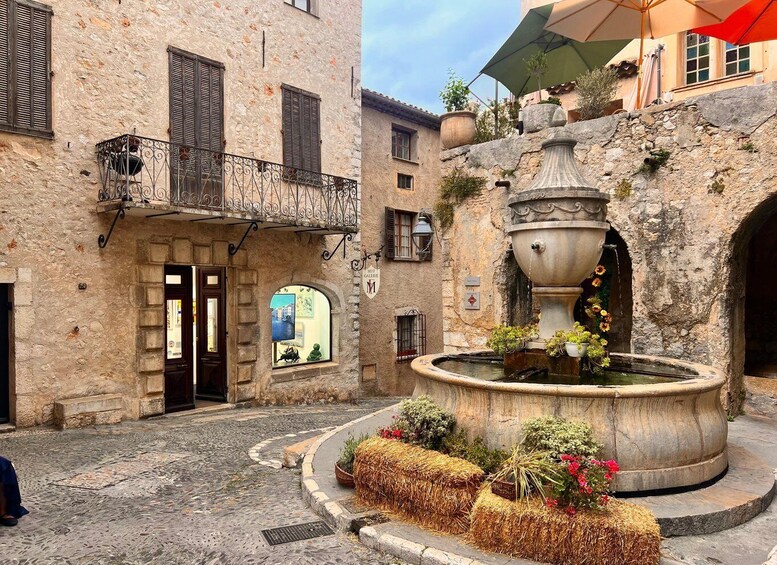 A stone building with a balcony, a fountain with flowers, and a cobblestone street. 2