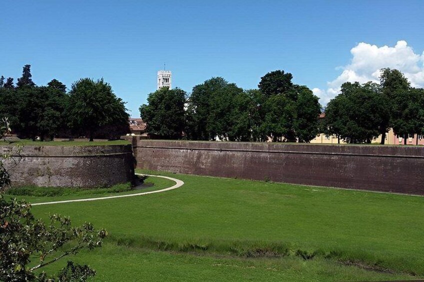 A grassy area with a curved path, a stone wall, and a tower in the distance. 1