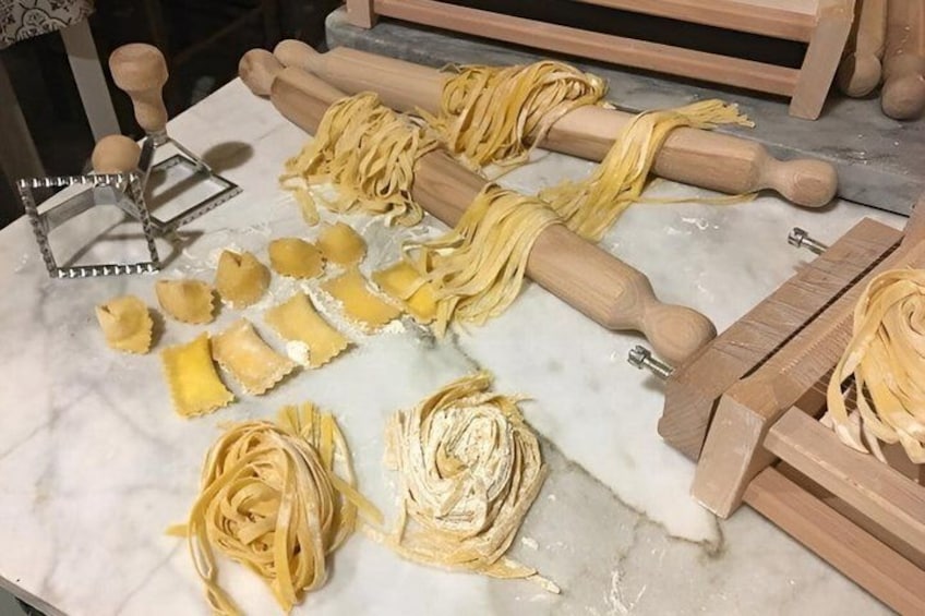 Pasta sheets, wooden pasta rollers, and a metal pasta cutter on a marble surface. 3