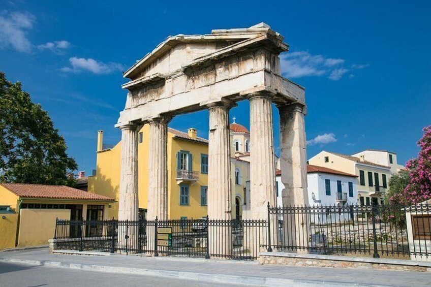 A classical Greek temple with columns, surrounded by modern buildings and a clear blue sky. 4