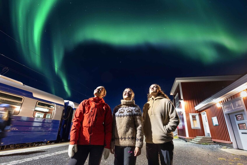Three people standing at a train station with the aurora borealis in the background. 1