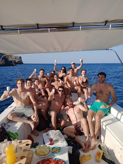 A group of people on a boat with drinks, surrounded by water and a rocky coastline. 3
