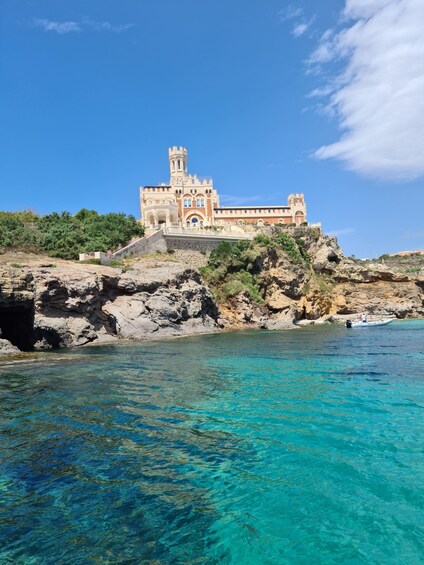 A castle on a rocky coastline with clear blue waters. 2