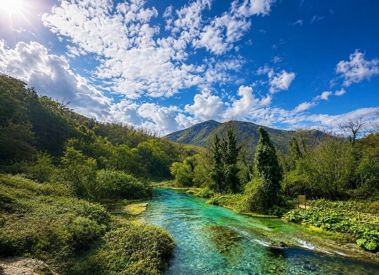 A clear river winding through a lush valley with mountains in the background and a partly cloudy sky. 1