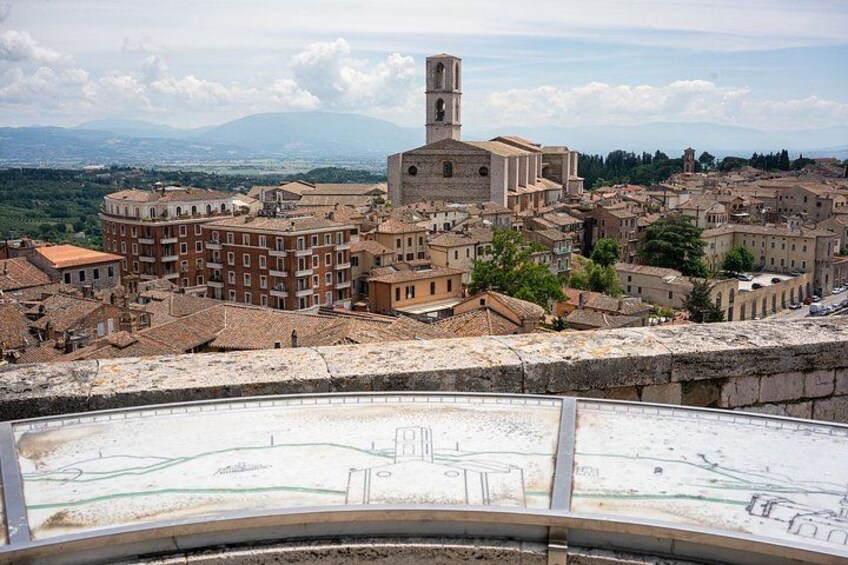 A historic town with a prominent church tower, terracotta-roofed buildings, and a view of the surrounding landscape. 1