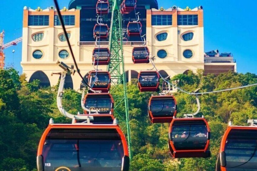 A cable car system with multiple gondolas ascending a cable, a large building with circular windows, and greenery in the foreground. 5
