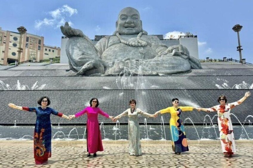 A group of people holding hands in front of a large Buddha statue with water fountains. 1