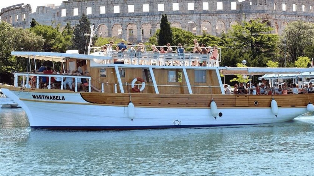 A boat named MARTINABELLA docked near a historic building with tourists on board. 1