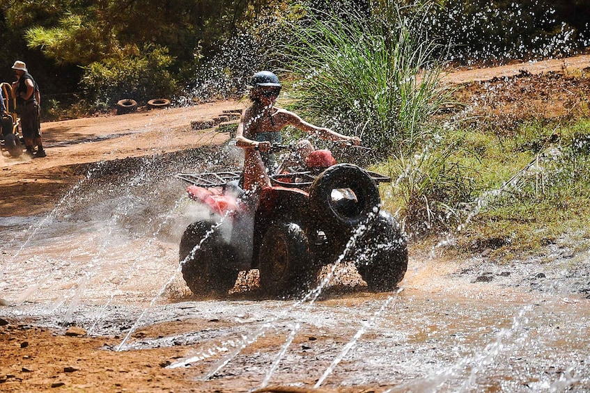 A person riding a quad bike through a muddy area, splashing water. 2