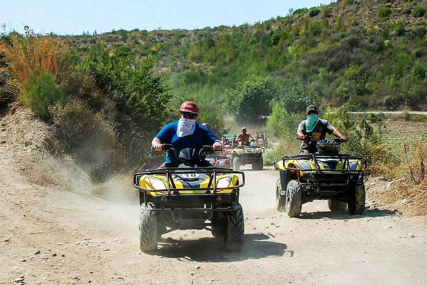 Two people riding ATVs on a dirt road with vegetation on the sides. 4