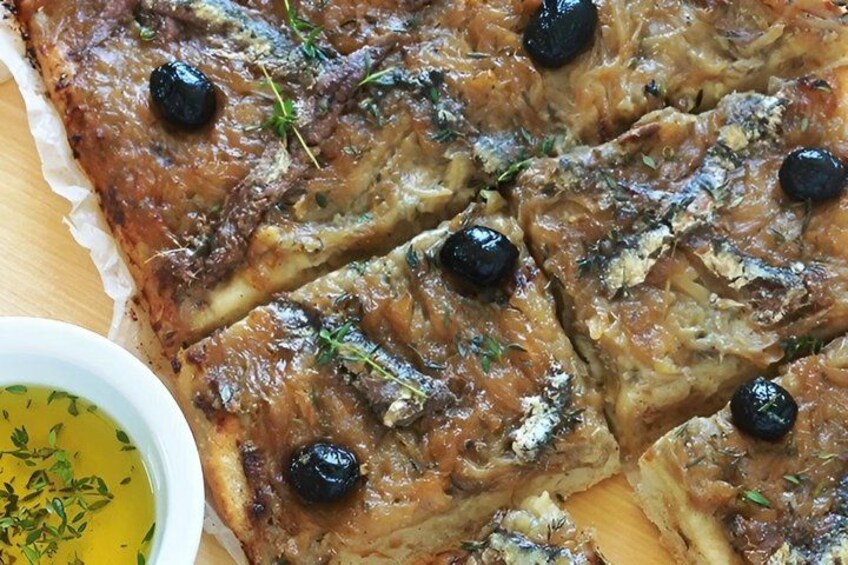 A baked dish with black olives and herbs, accompanied by a small bowl of sauce. 3