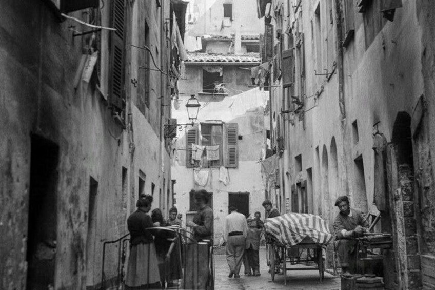 A narrow street with buildings, a street lamp, and a person carrying a large striped cloth. 2
