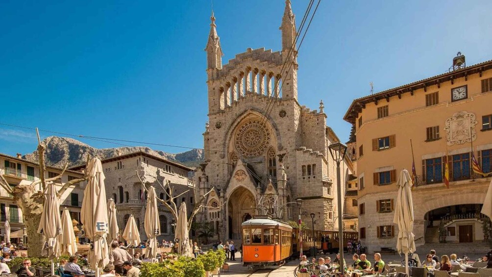 A historic cathedral with intricate architecture, a tram in the foreground, and outdoor seating areas with umbrellas. 2