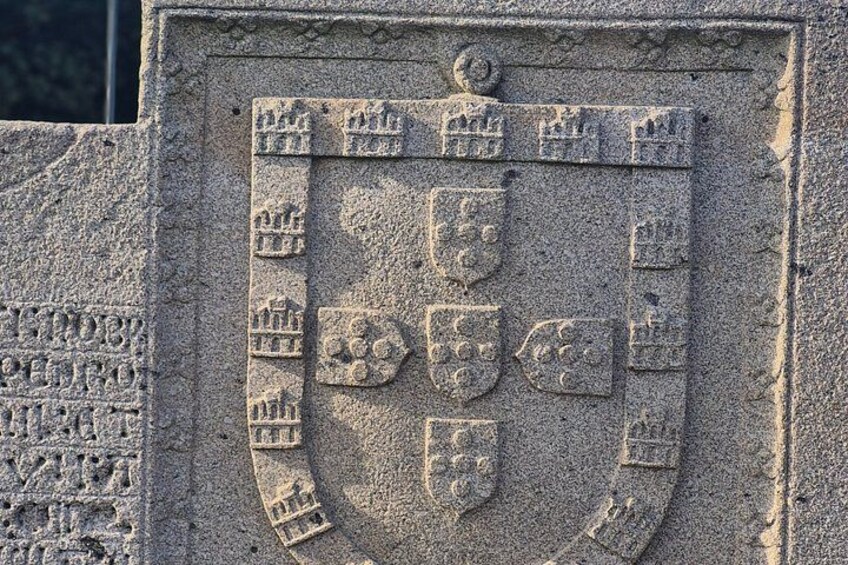 A stone monument with a coat of arms featuring shields and a crest. 3