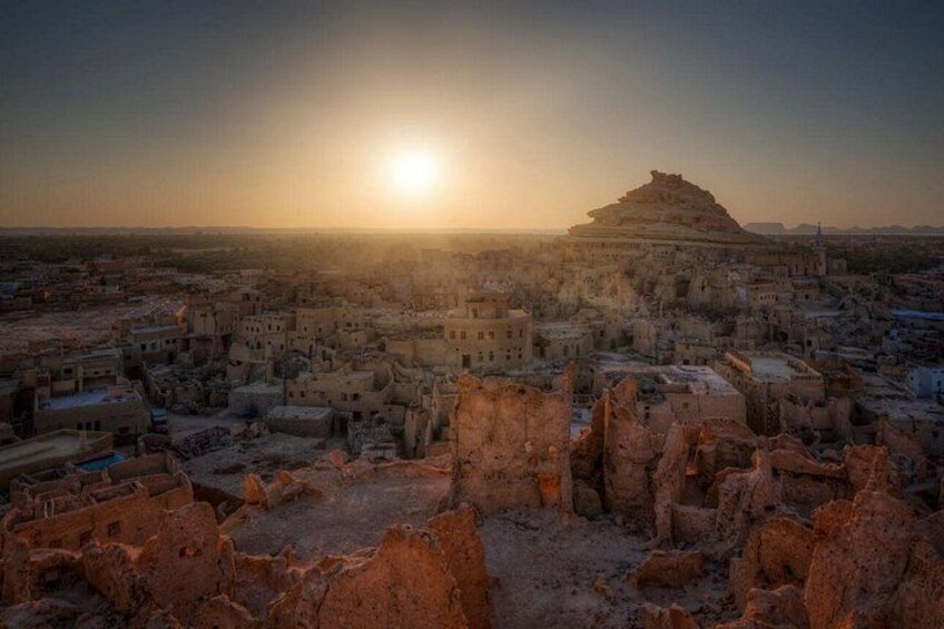 A desert cityscape at sunset with ancient ruins and a prominent hilltop structure. 5