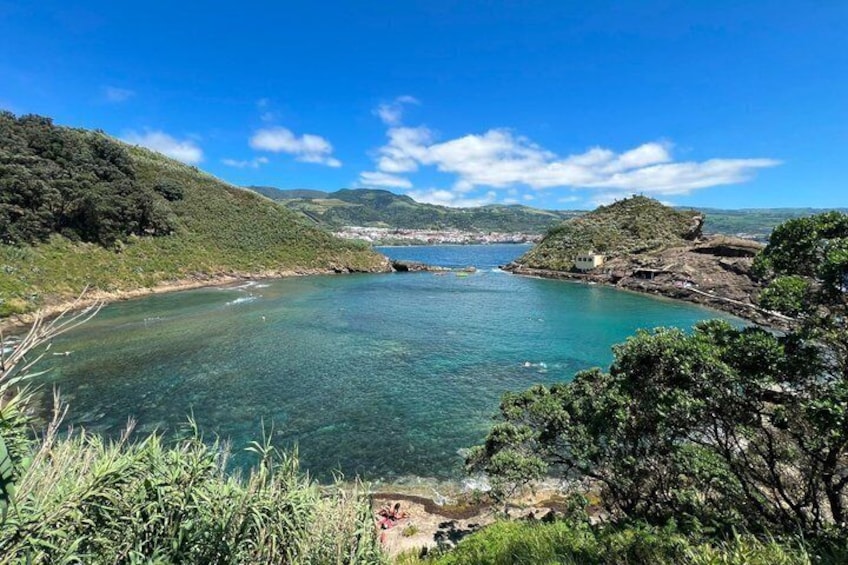 A coastal landscape with clear water, green hills, and a small building on a hill. 2