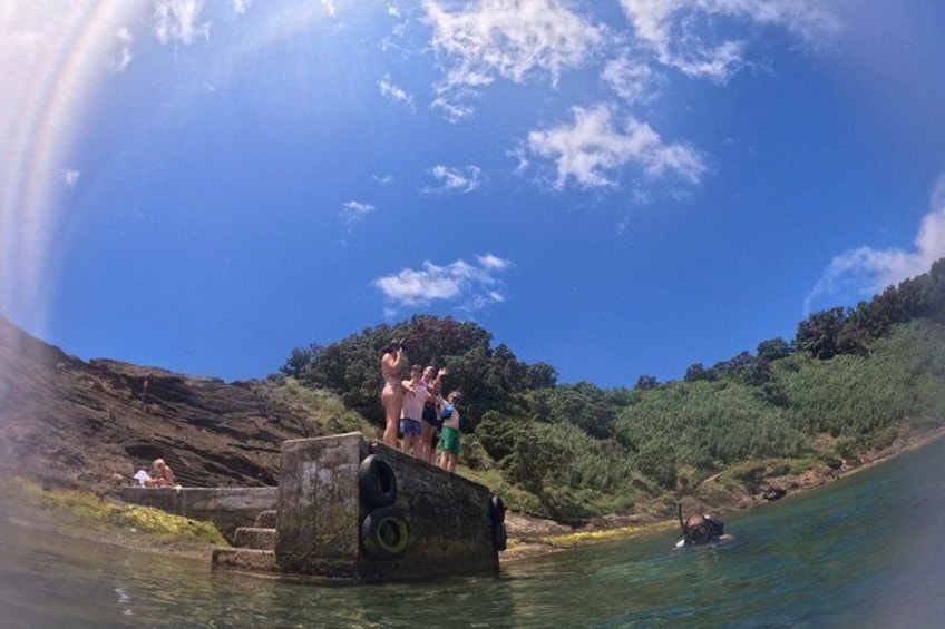 A group of people on a concrete platform by a river, with a forested hill in the background. 4