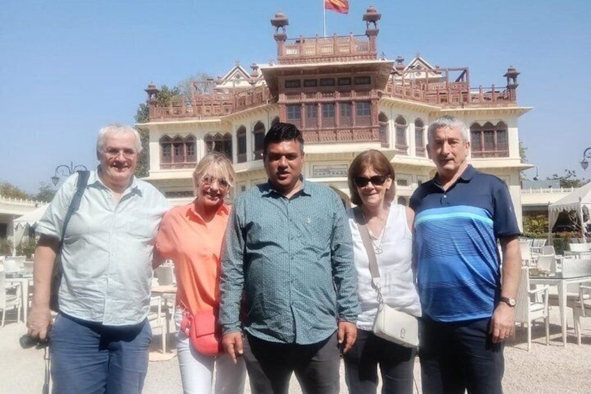 A group of people standing in front of a large, ornate building with a flag on top. 2