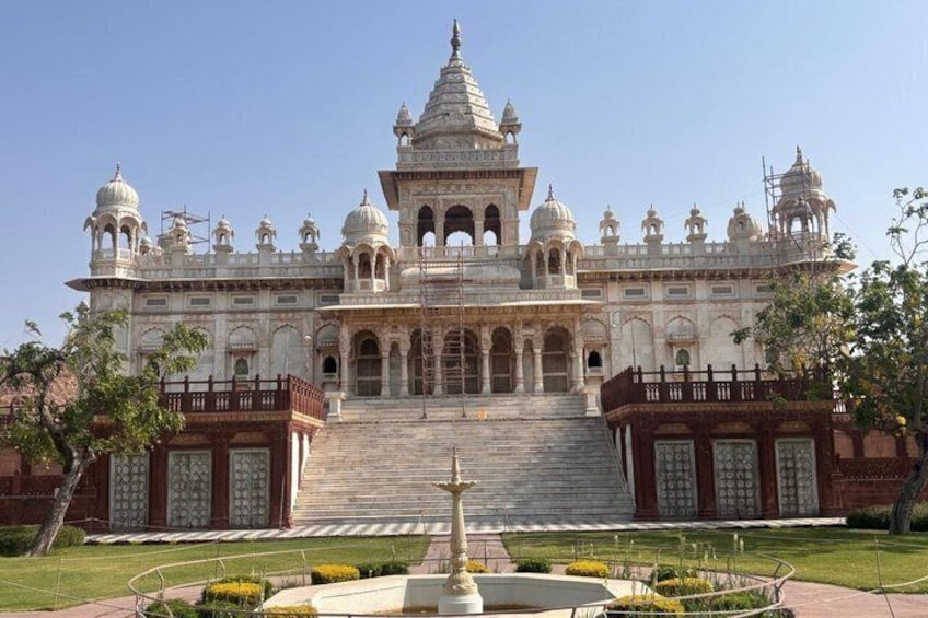 A large, ornate building with multiple domes and arches, surrounded by a well-maintained garden and a clear sky. 1