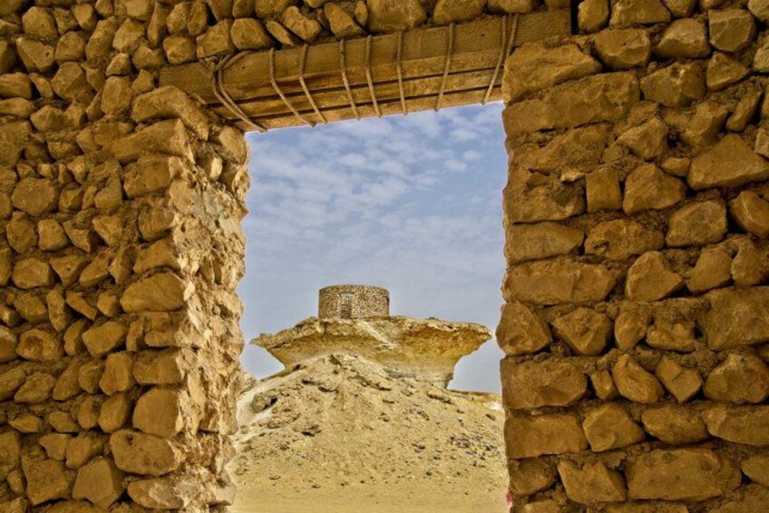 A stone archway framing a view of a desert landscape with a mound and a small structure on top. 2