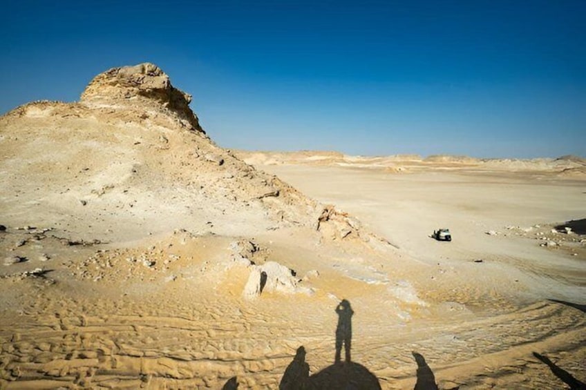 A desert landscape with a prominent sand dune, a vehicle, and a person standing on the dune. 5