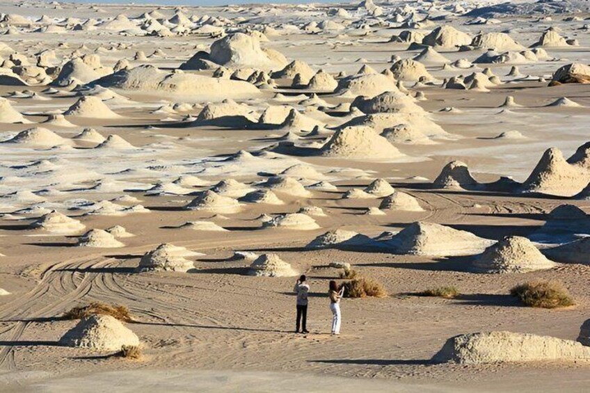 A vast desert landscape with numerous sand formations and two people standing in the foreground. 1
