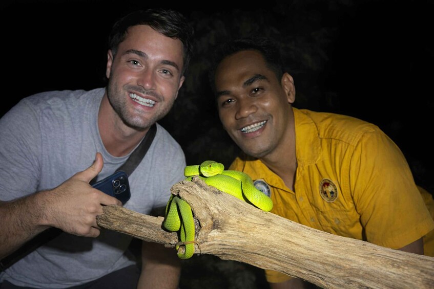 Two people holding a branch with a green snake on it. 3