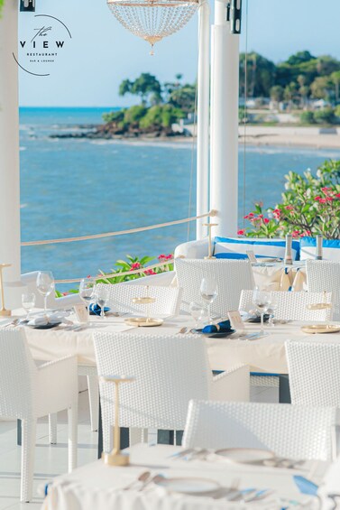 A seaside restaurant with white wicker chairs and tables set for dining. 4