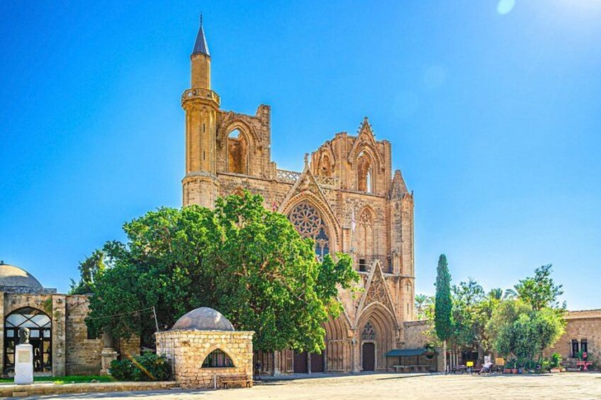 A historic cathedral with a tall bell tower, intricate Gothic architecture, and lush green trees in the foreground. 1
