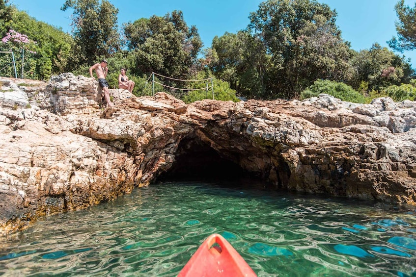 A rocky cave entrance with clear water, a rope bridge, and people near the entrance. 5