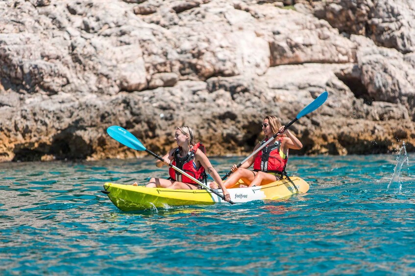 Two people kayaking on a calm body of water with rocky cliffs in the background. 2