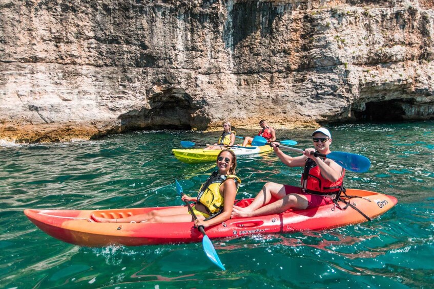 People kayaking on clear water with rocky cliffs in the background. 1